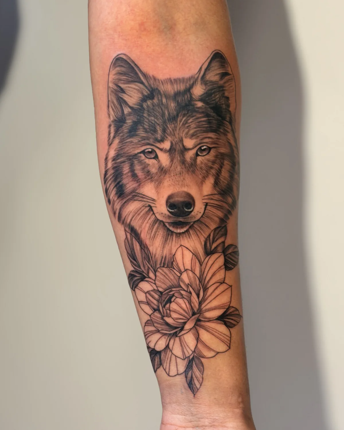 Tatuagem fine line de lobo com peônia no antebraço, traço fino em preto e cinza